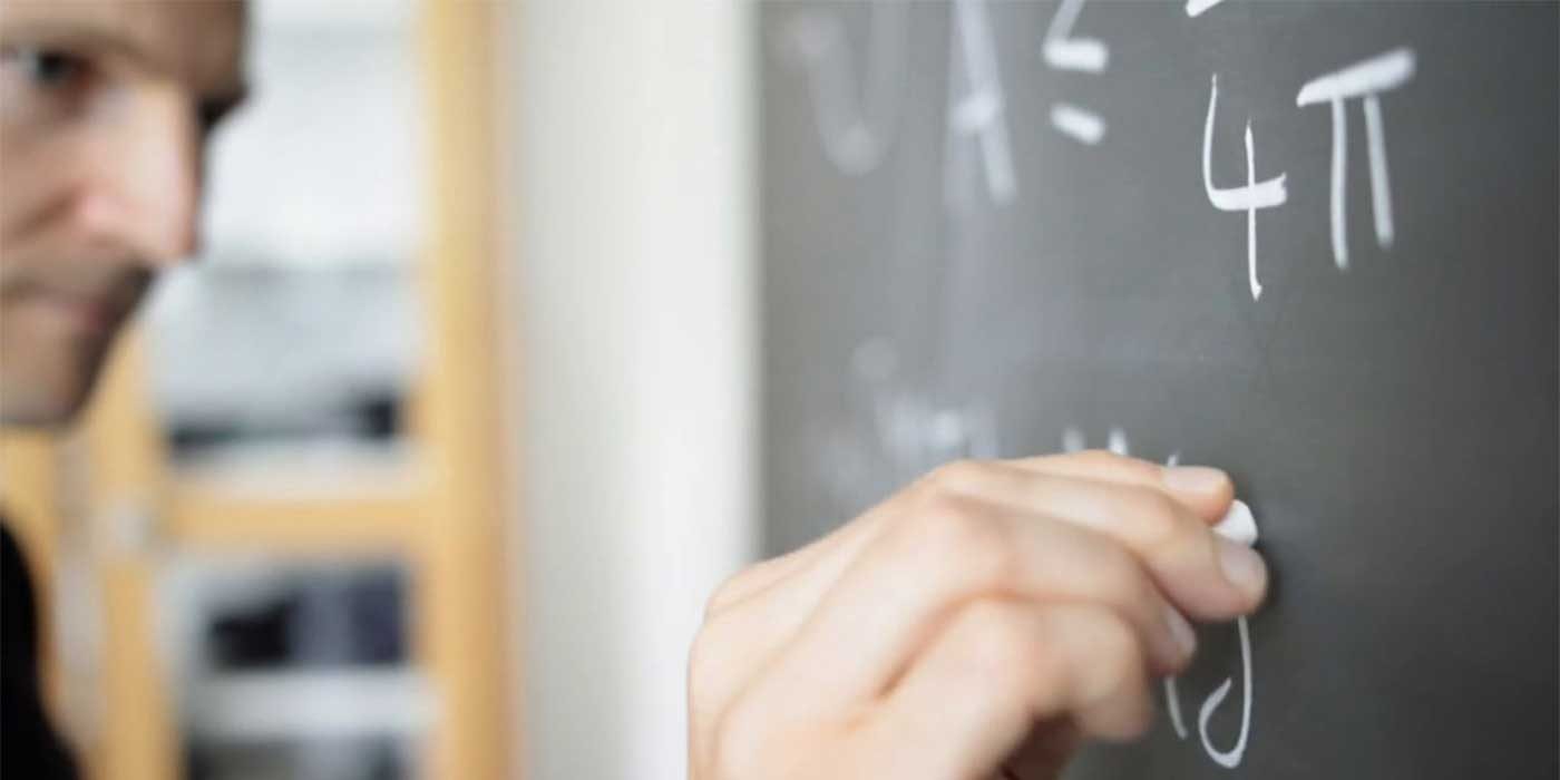 Photo of a teacher writing maths equations on a blackboard