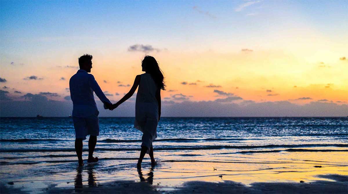 Photo of a bride and groom walking on a beach at sunset on their honeymoon